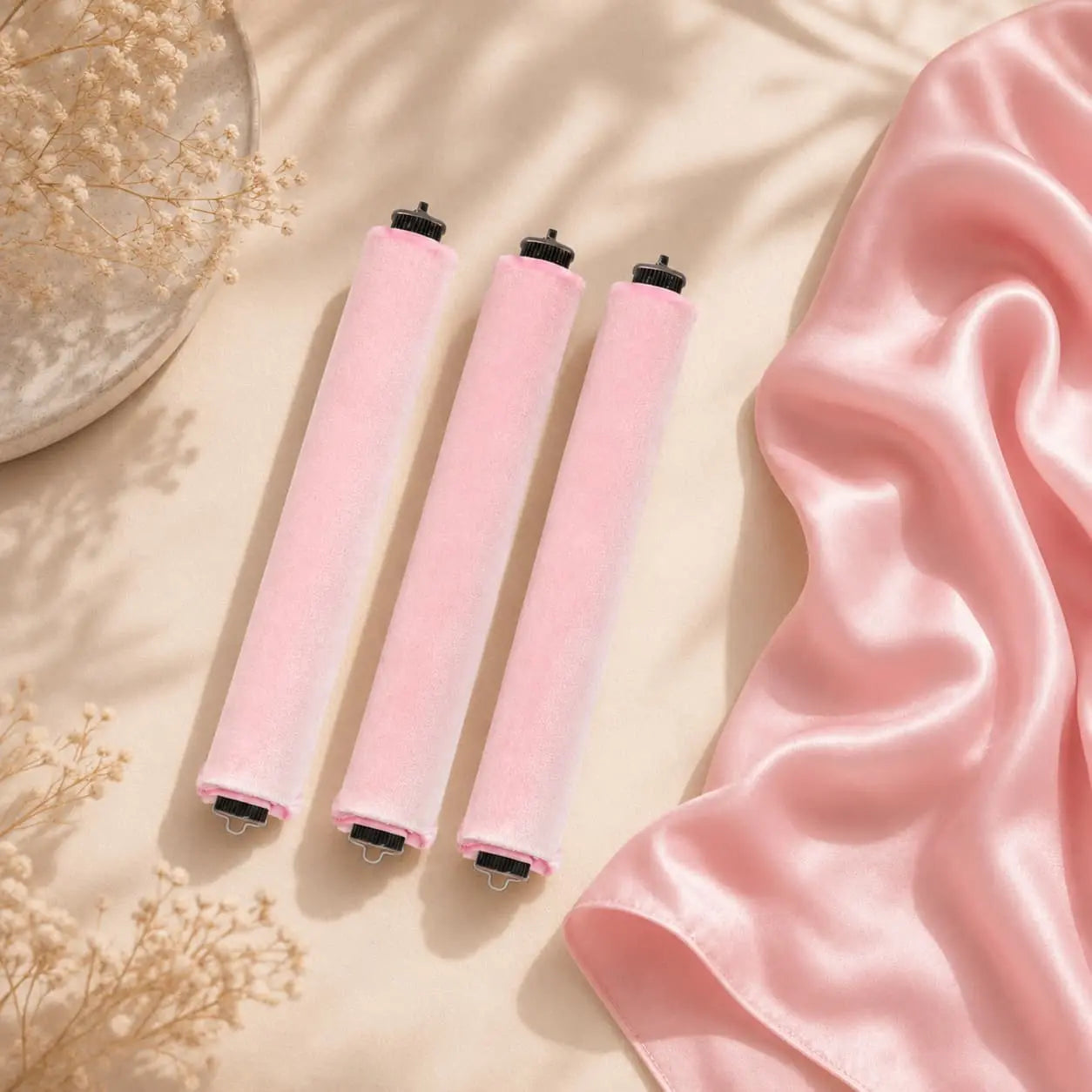 Three pink velvet heatless curlers beside a pink satin scarf.