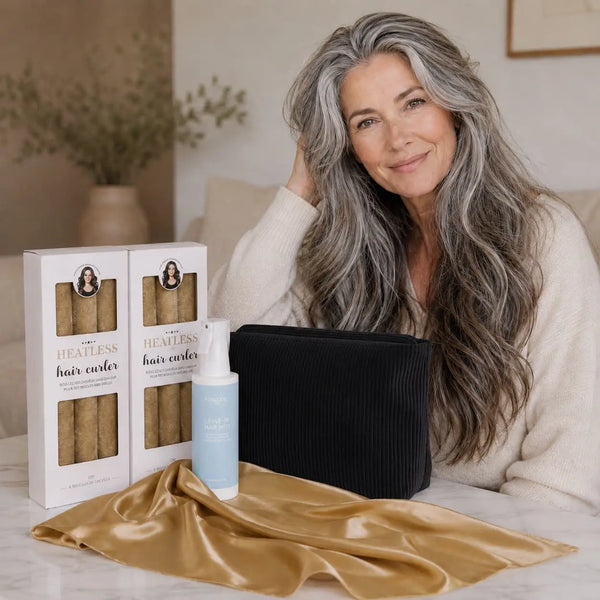Woman over 60 with long thick hair presenting the Long Hair Curl Essentials Gold Set with heatless curlers, hair mist, satin scarf and black storage pouch