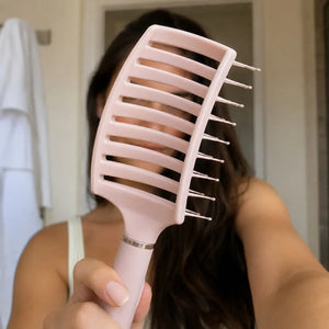 Woman holding a pale pink anti-static vent brush for detangling and blow-drying hair.