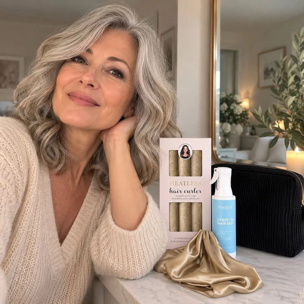 Mature woman with shoulder-length silver blonde wavy hair showcasing beige heatless curlers, leave-in hair mist, black cosmetic pouch and champagne satin bonnet.