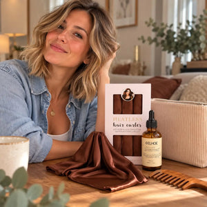 Woman with shoulder-length blonde wavy hair showcasing brown heatless curlers, hair serum, beige cosmetic pouch, brown satin bonnet and wooden wide-tooth comb.
