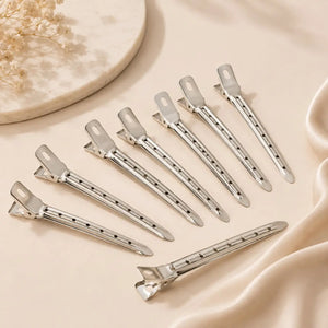 Silver metal hair clips arranged on a neutral satin background for securing volume hair rollers during blowout styling.