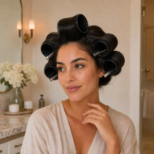 Woman wearing black volume hair rollers secured with metal clips to create lift, body and a blowout-style finish.